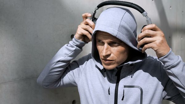 Model in grauem Hoodie der Porsche Design Performance Kollektion mit Kopfhörern vor Betonwand, Szenenbild aus dem Produktfilm, produziert von der Filmproduktion erdmann & erdmann aus Hanau