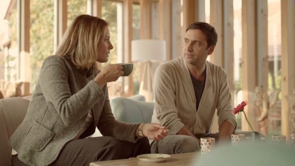 Zwei Gäste bei entspanntem Gespräch mit Tee in lichtdurchflutetem Holzhaus, Szenenbild aus dem Imagefilm des Rosenberg Ayurveda Kurzentrums, produziert von der Filmproduktion erdmann & erdmann aus Hanau